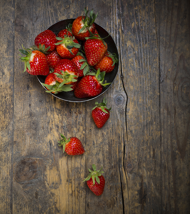 Metal bowl of strawberries on dark wood, view from above